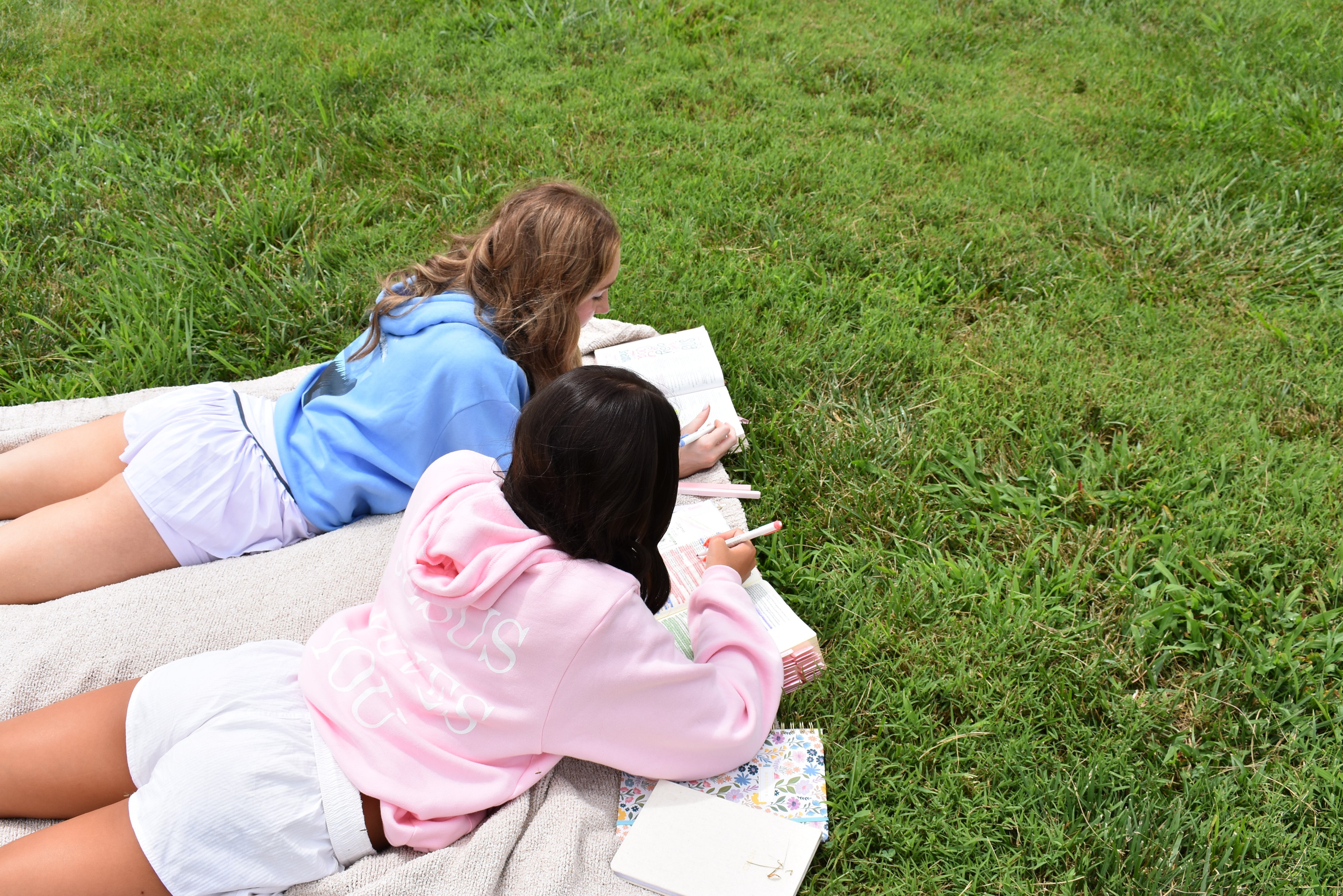 Two girls studying the Bible together on a blanket in the grass