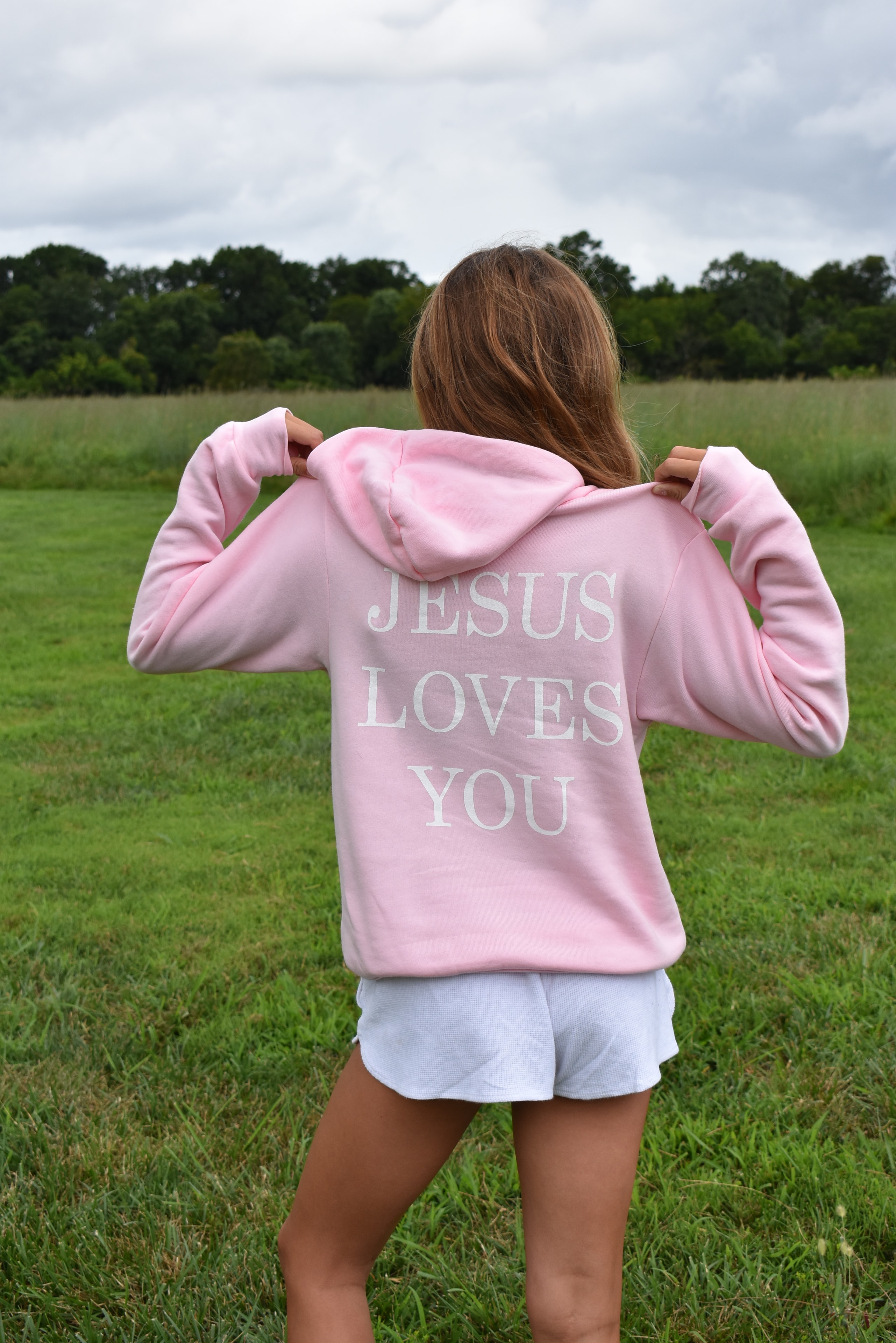 Girl wearing Jesus Loves You hoodie in a field